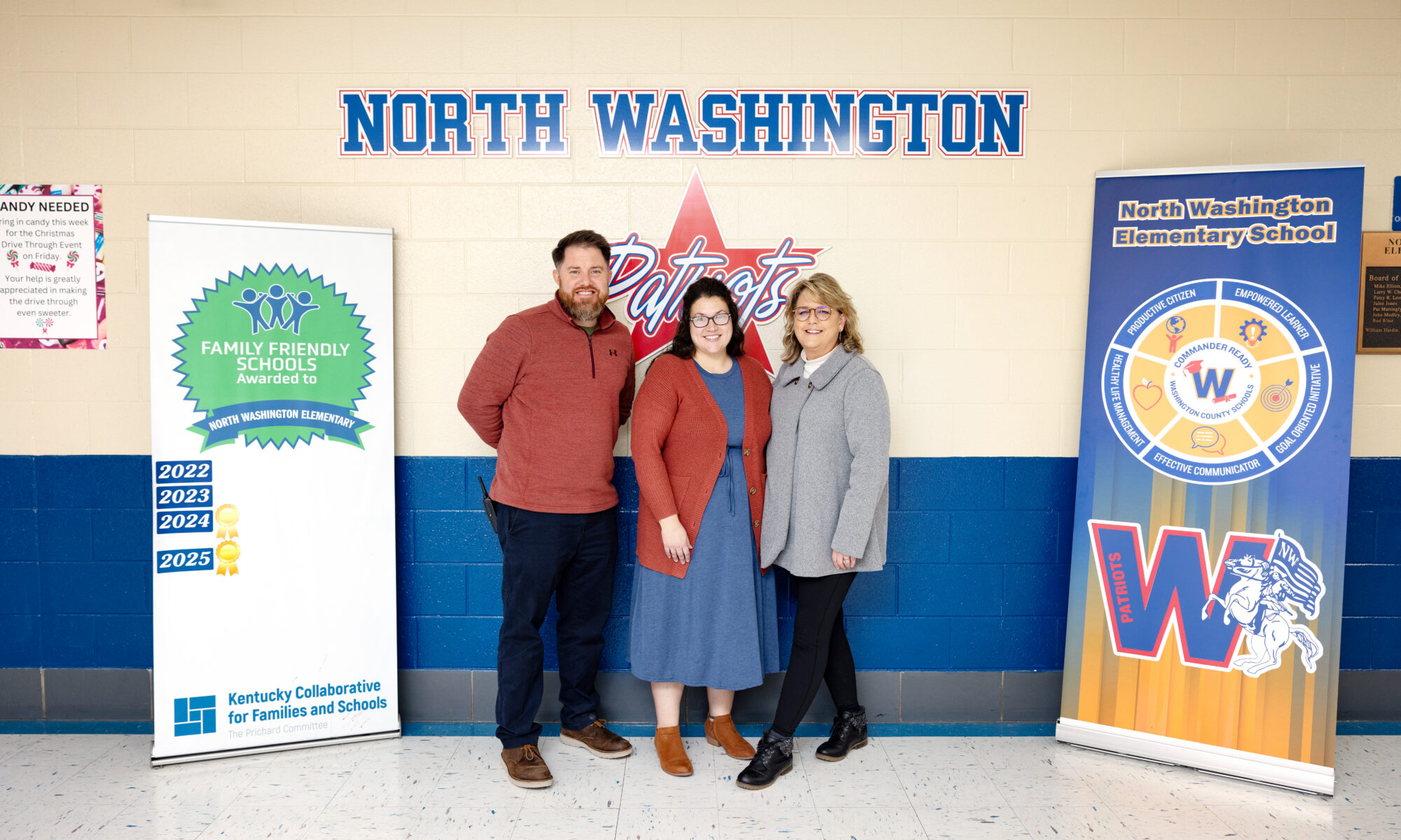 A principal, parent, and district staff member stand by their Family Friendly School Certification poster.