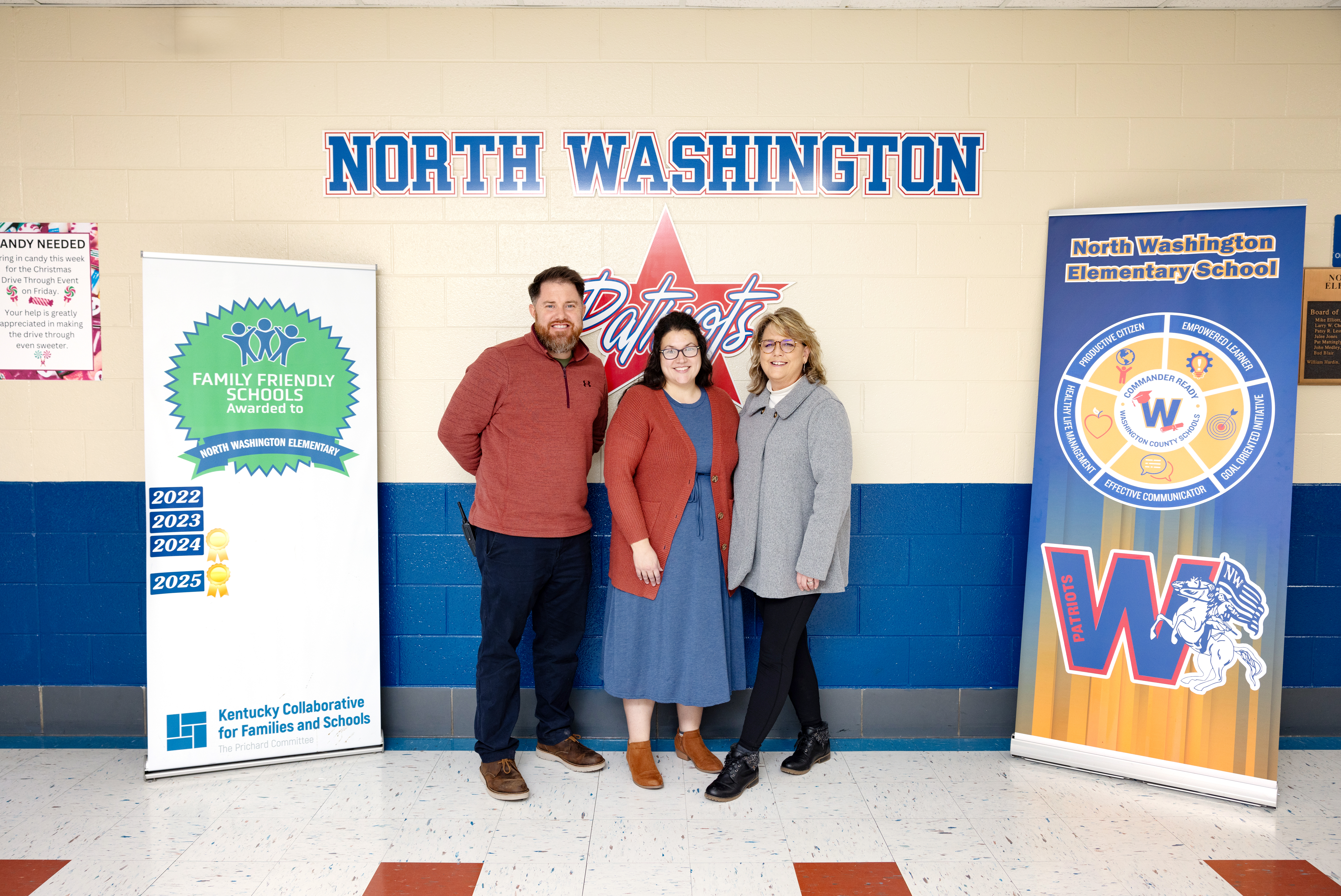 A principal, parent, and district staff member stand by their Family Friendly School Certification poster.